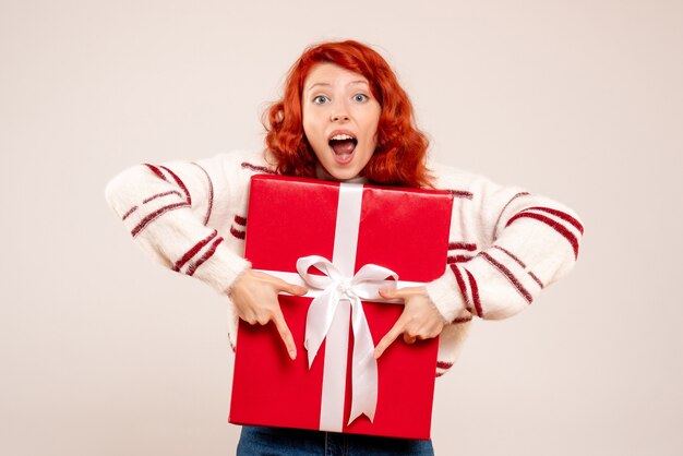 Front view of young woman with big present on white wall