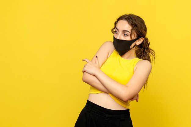 Front view of young woman with black mask on yellow wall