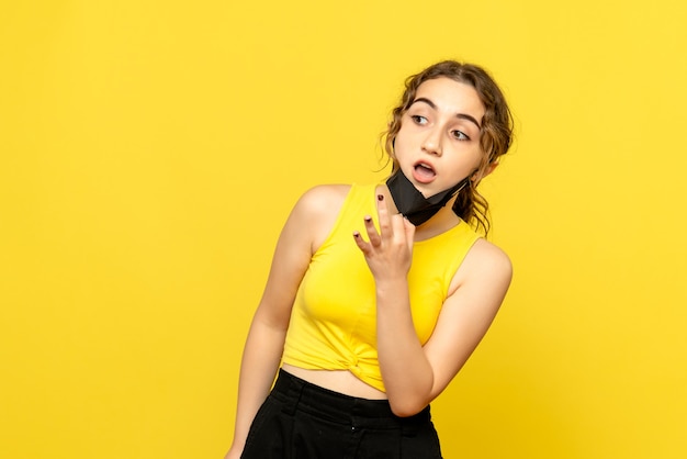 Front view of young woman with black mask on yellow wall