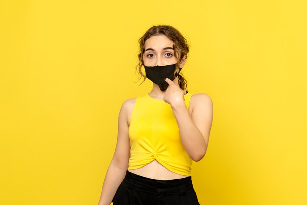 Front view of young woman with black mask on yellow wall