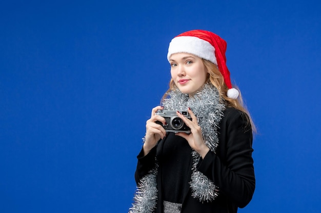 Front view of young woman with camera on blue wall