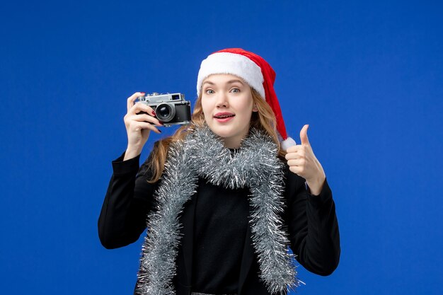 Front view of young woman with camera on blue wall