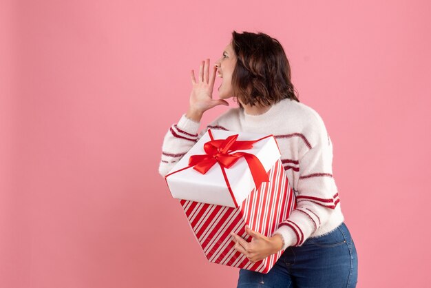 Front view of young woman with christmas present calling on pink wall