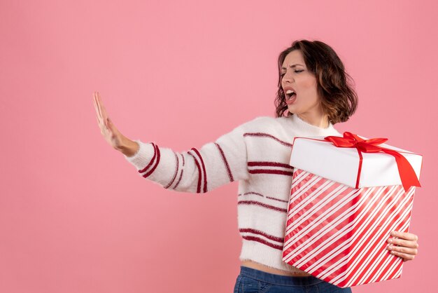 Front view of young woman with christmas present displeased on pink wall