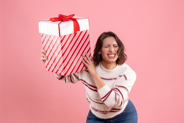 Front view of young woman with christmas present on a pink wall