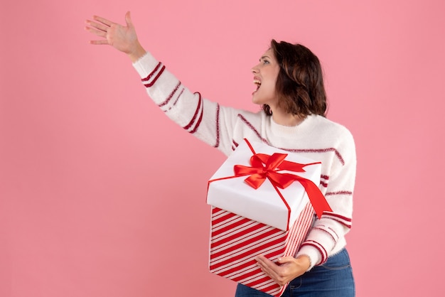 Front view of young woman with christmas present on pink wall