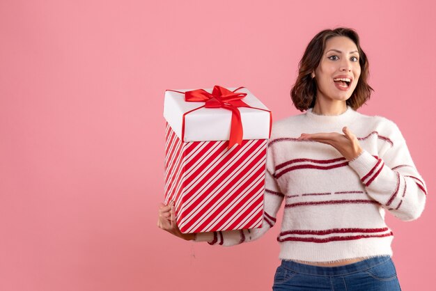 Front view of young woman with christmas present on pink wall