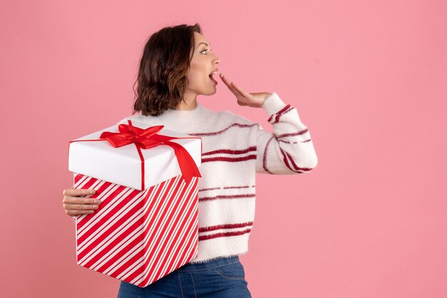 Front view of young woman with christmas present on pink wall