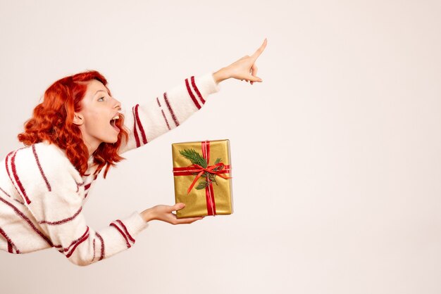 Front view of young woman with christmas present on the white wall