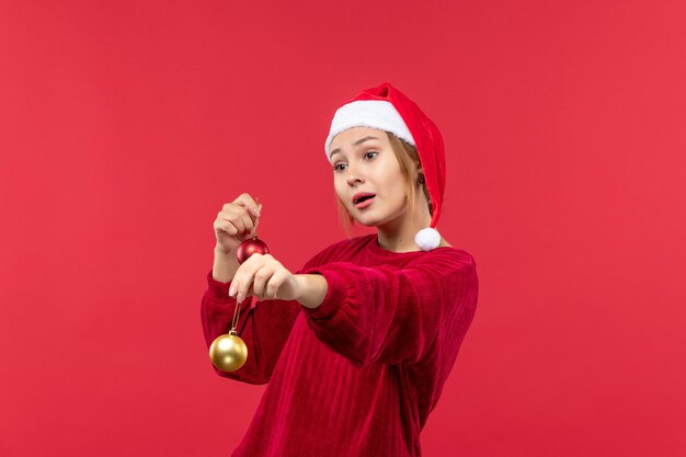 Вид спереди молодая женщина с рождественскими игрушками на красном полу рождественские праздничные эмоции