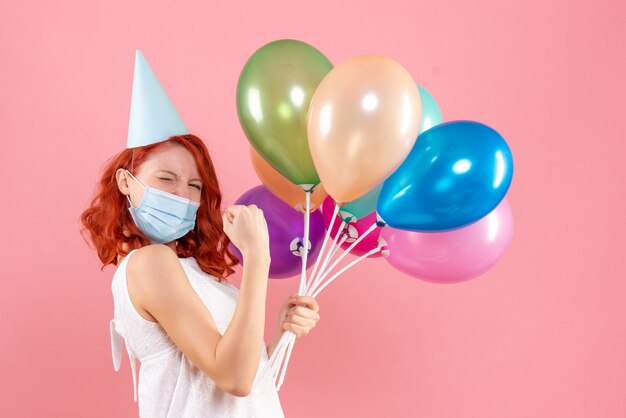 Free photo front view of young woman with colorful balloons in sterile mask on the pink wall