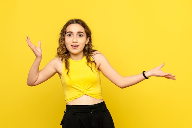 Front view of young woman with confused expression on yellow wall