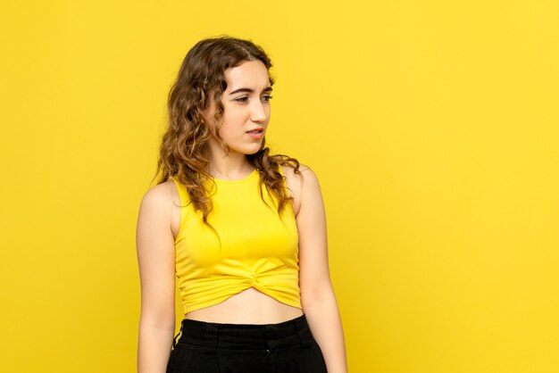 Front view of young woman with confused expression on yellow wall