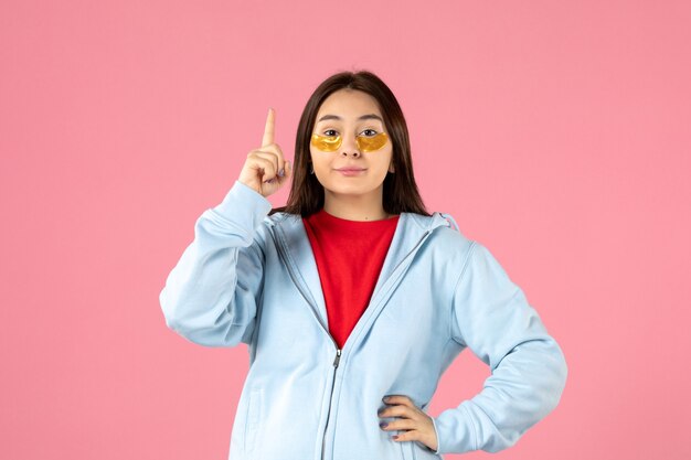 front view of young woman with eye patches under her eyes on pink wall