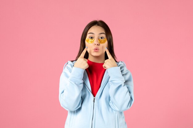 front view of young woman with eye patches under her eyes on pink wall