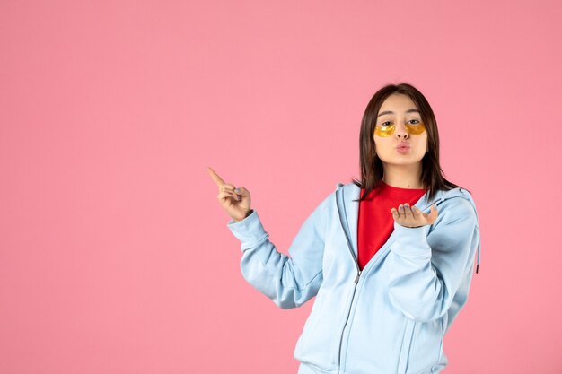 front view of young woman with eye patches under her eyes on pink wall