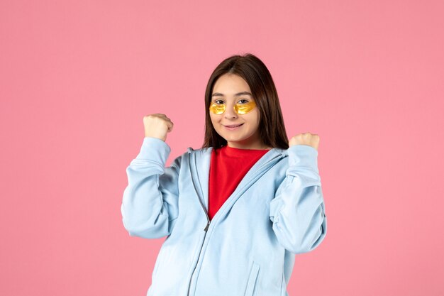 front view of young woman with eye patches under her eyes on pink wall