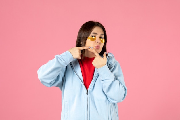 Vista frontale della giovane donna con le bende sull'occhio sotto gli occhi sul muro rosa