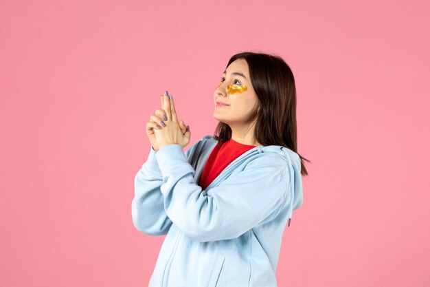 front view of young woman with eye patches under her eyes on pink wall