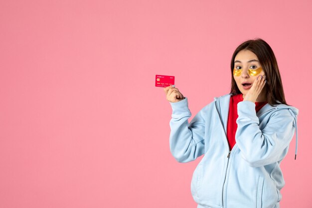 Foto gratuita vista frontale della giovane donna con le bende sull'occhio che tiene la carta di credito sulla parete rosa