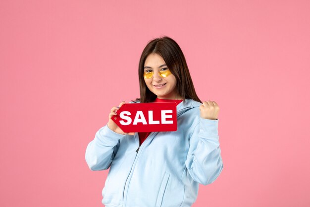 front view of young woman with eye patches holding sale banner on pink wall