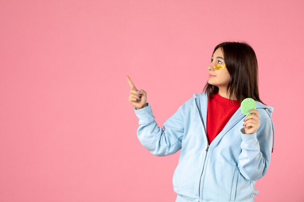 front view of young woman with eye patches and little skin sponge on pink wall