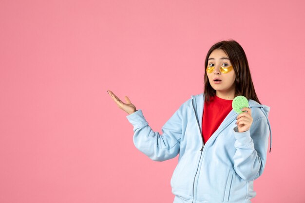 front view of young woman with eye patches and little skin sponge on pink wall