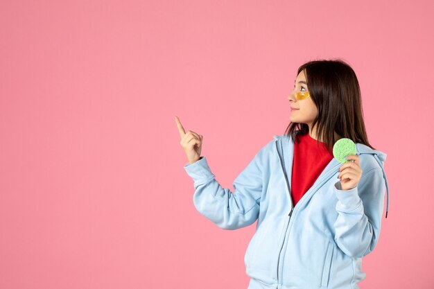 front view of young woman with eye patches and little skin sponge on pink wall