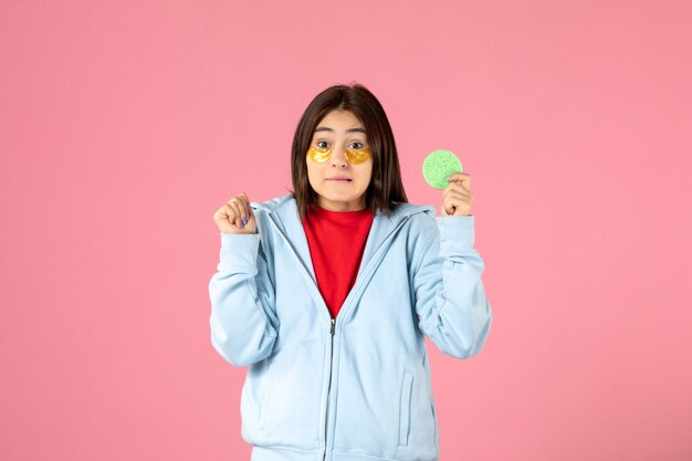 front view of young woman with eye patches and little sponge on pink wall