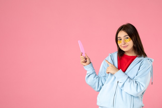 front view of young woman with eye patches and nail file on pink wall