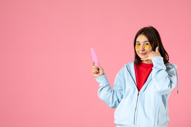 front view of young woman with eye patches and nail file on pink wall