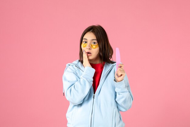 front view of young woman with eye patches and nail file on pink wall