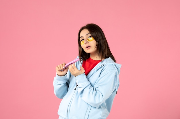 front view of young woman with eye patches and nail file on pink wall