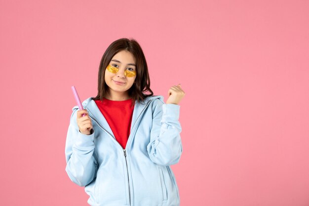 front view of young woman with eye patches and nail file on pink wall