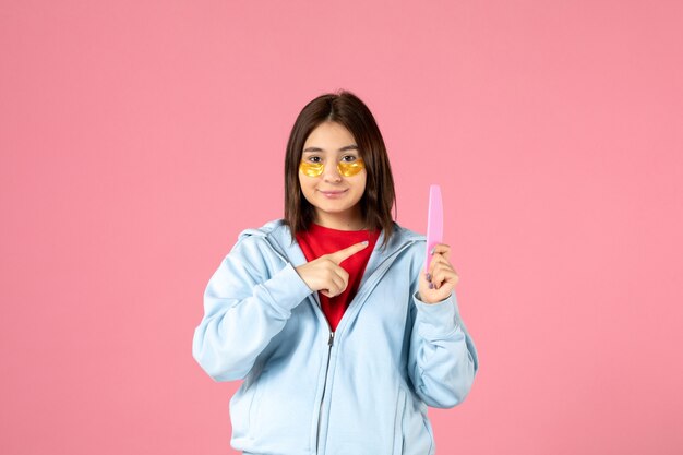 front view of young woman with eye patches and nail file on pink wall