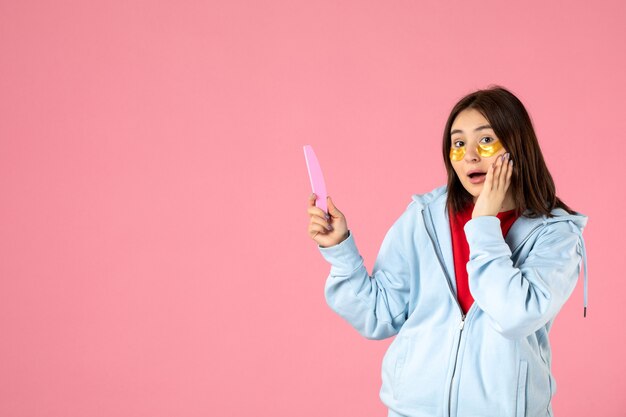 Vista frontale della giovane donna con bende per gli occhi e lima per unghie sul muro rosa