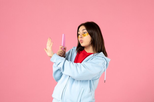 front view of young woman with eye patches and nail file on pink wall