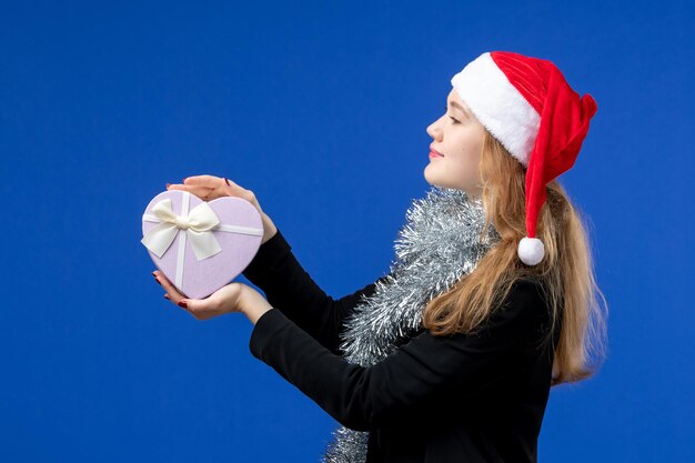 Front view of young woman with holiday present on blue wall