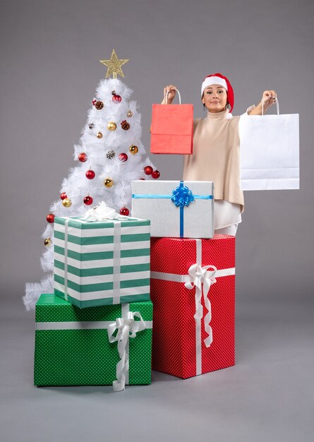 Вид спереди молодая женщина с праздничными подарками на сером столе новогодний рождественский подарок