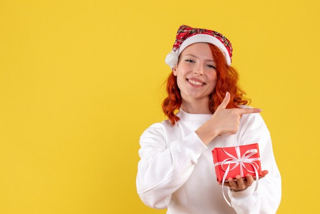 Front view of young woman with little xmas present on yellow wall