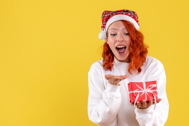 Front view of young woman with little xmas present on yellow wall