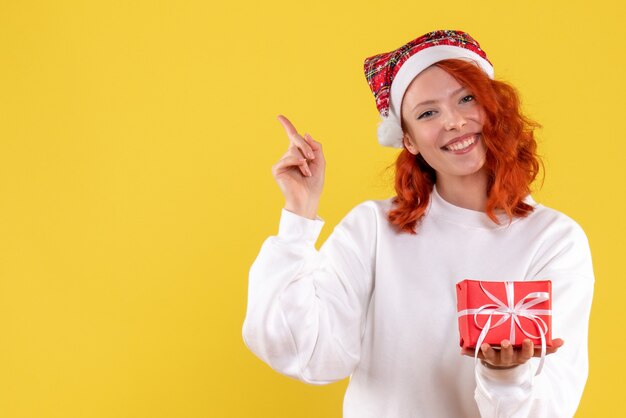 Front view of young woman with little xmas present on yellow wall