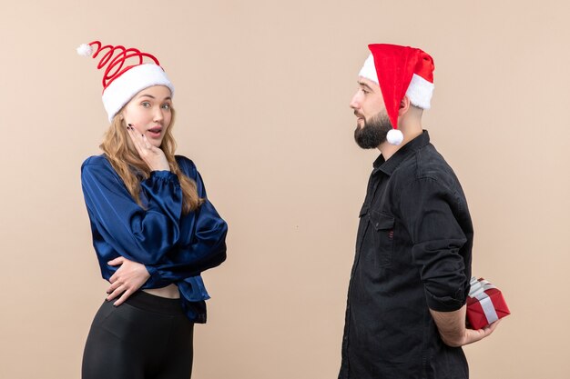 Front view of young woman with man who's preparing to give her a present on pink wall