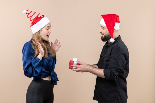 Front view of young woman with man who's preparing to give her a present on pink wall