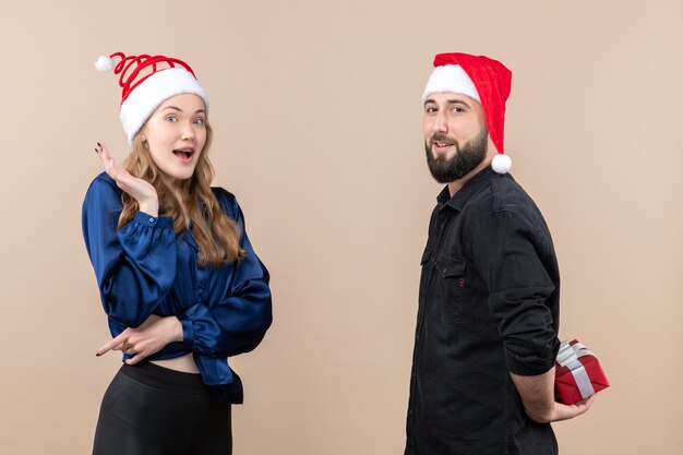 Front view of young woman with man who's preparing to give her a present on pink wall