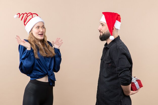 Front view of young woman with man who's preparing to give her a present on the pink wall