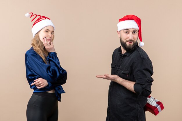 Front view of young woman with man who's preparing to give her a present on the pink wall