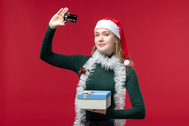 Молодая женщина вид спереди с подарком и банковской картой на красном фоне