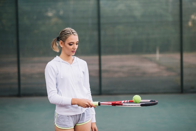 Бесплатное фото Вид спереди молодая женщина с ракеткой и мячом для тенниса