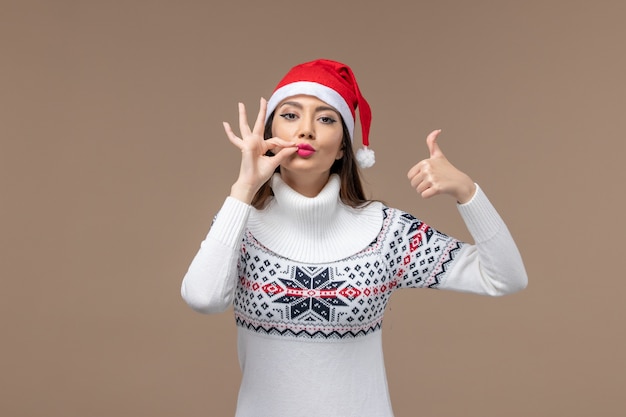 Вид спереди молодая женщина с красной рождественской шапкой на коричневом фоне рождественские эмоции новый год